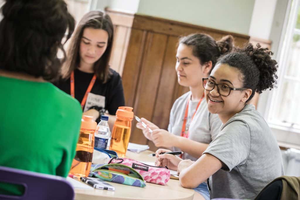 Oxford Uluslararası Konaklama Merkezi’nde bir masanın etrafında sohbet eden, boyun askısı takmış öğrenciler