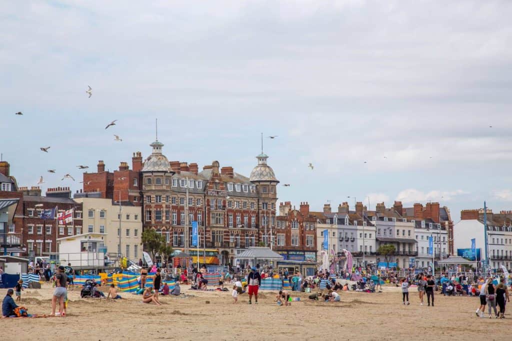 Ein überfüllter Sandstrand und Gebäude an der Strandpromenade in Weymouth an einem Sommertag