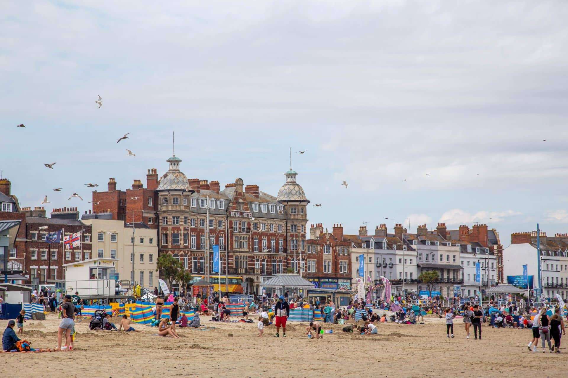 Ein überfüllter Sandstrand und Gebäude an der Strandpromenade in Weymouth an einem Sommertag